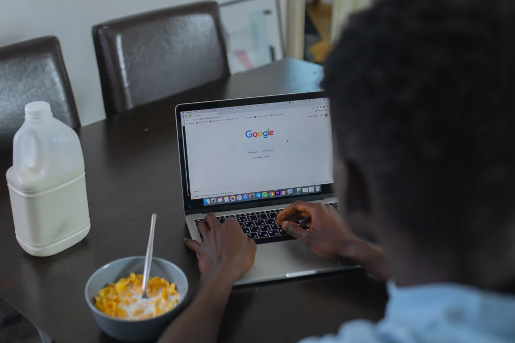 A man working on his laptop computer while eating cereal. The laptop screen shows a Google Ads conversion campaign