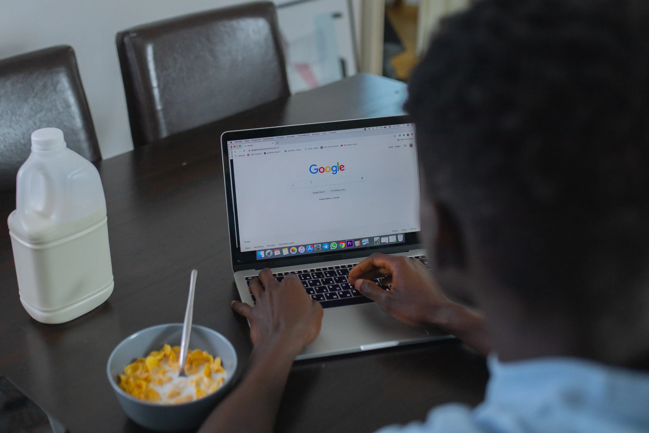 A man working on his laptop computer while eating cereal. The laptop screen shows a Google Ads conversion campaign